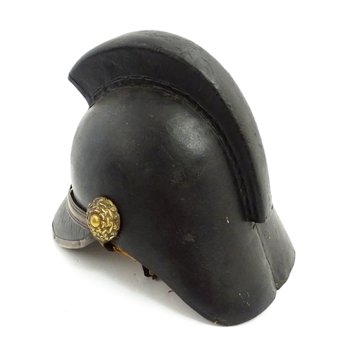 1469 - A 19thC fireman's helmet, the black leather shell with visor and rear brim, decorated with cockades,... 