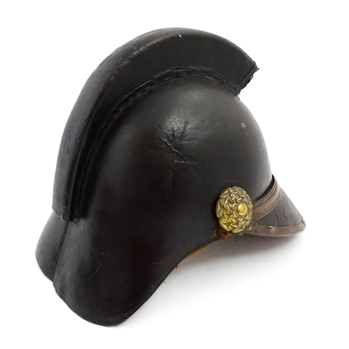 1469 - A 19thC fireman's helmet, the black leather shell with visor and rear brim, decorated with cockades,... 