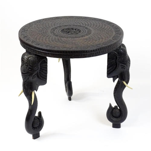 1804 - An early 20thC Anglo Indian occasional table with a carved, scrolled top above four elephant formed ... 