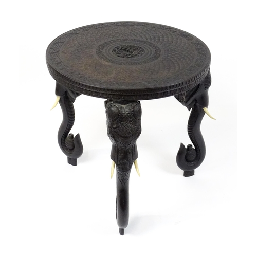 1804 - An early 20thC Anglo Indian occasional table with a carved, scrolled top above four elephant formed ... 