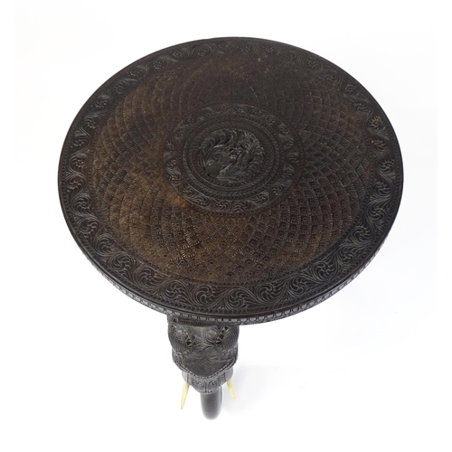 1804 - An early 20thC Anglo Indian occasional table with a carved, scrolled top above four elephant formed ... 