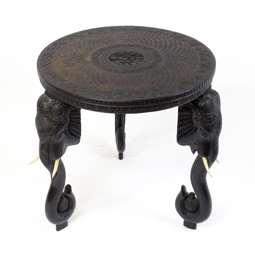 1804 - An early 20thC Anglo Indian occasional table with a carved, scrolled top above four elephant formed ... 