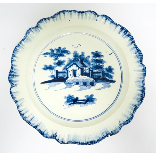 63 - An English blue and white plate with feather edge with hand painted decoration depicting a cottage i... 