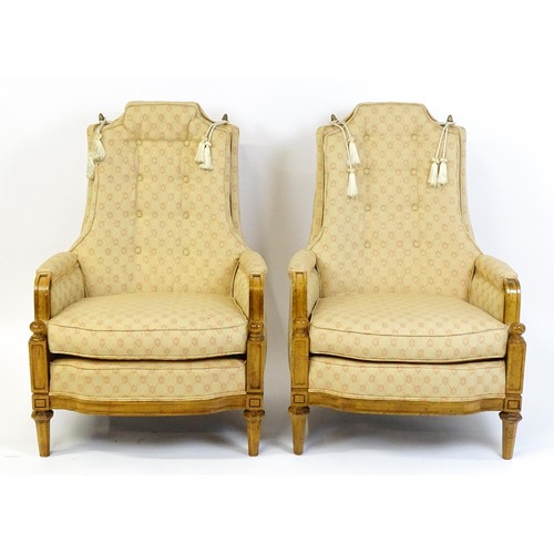 1831 - A pair of  20thC armchairs surmounted by brass finials, the chairs having deep buttoned cushions, in... 