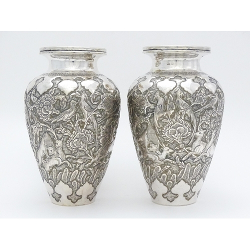 487 - A pair of Iranian / Persian silver vases decorated in relief with animals, birds and flowers. Possib... 