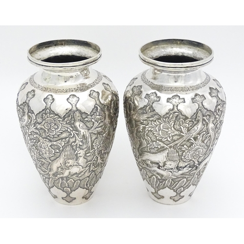 487 - A pair of Iranian / Persian silver vases decorated in relief with animals, birds and flowers. Possib... 