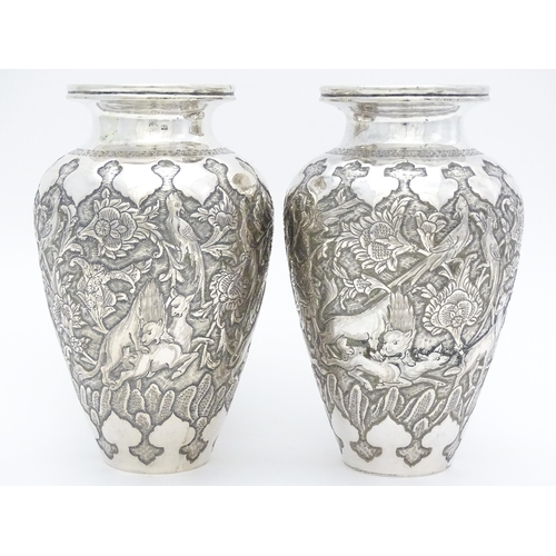 487 - A pair of Iranian / Persian silver vases decorated in relief with animals, birds and flowers. Possib... 