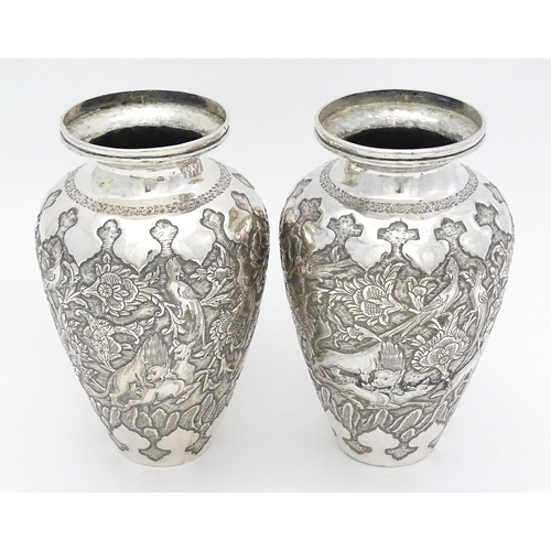 487 - A pair of Iranian / Persian silver vases decorated in relief with animals, birds and flowers. Possib... 