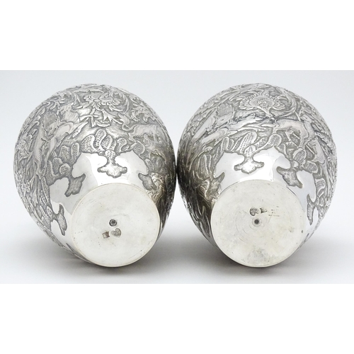 487 - A pair of Iranian / Persian silver vases decorated in relief with animals, birds and flowers. Possib... 