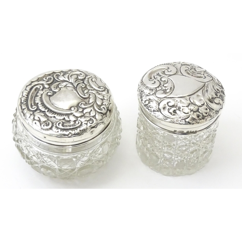 423 - Two cut glass dressing table jars with silver lids having embossed decoration, one hallmarked Birmin... 