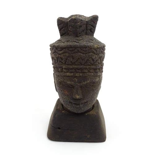 1045 - An Asian carved stone head of a deity with geometric and stylised feather headdress, raised on a tap... 