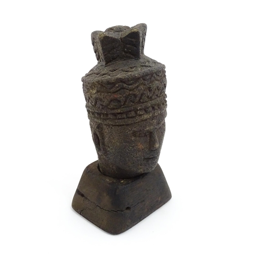 1045 - An Asian carved stone head of a deity with geometric and stylised feather headdress, raised on a tap... 