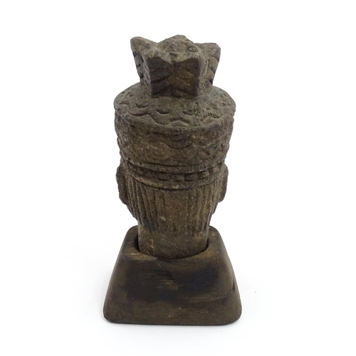 1045 - An Asian carved stone head of a deity with geometric and stylised feather headdress, raised on a tap... 