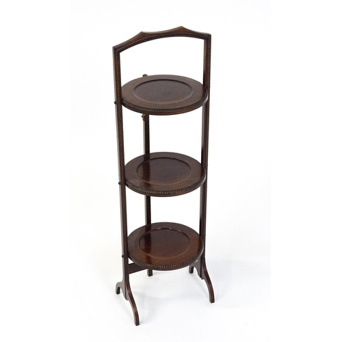 1481 - An early / mid 20thC mahogany folding cake stand, having three circular tiers with beadwork style mo... 