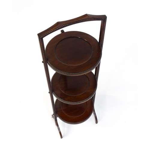 1481 - An early / mid 20thC mahogany folding cake stand, having three circular tiers with beadwork style mo... 