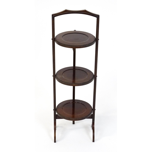 1481 - An early / mid 20thC mahogany folding cake stand, having three circular tiers with beadwork style mo... 