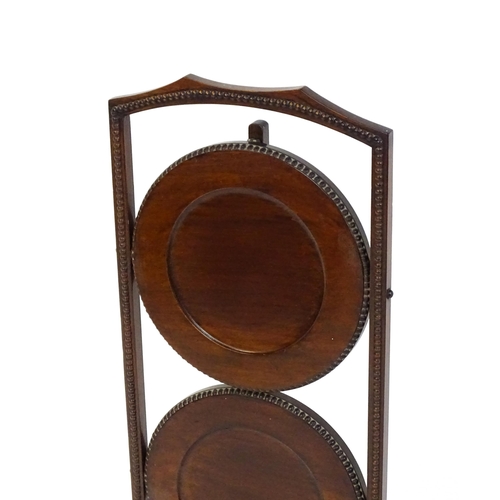 1481 - An early / mid 20thC mahogany folding cake stand, having three circular tiers with beadwork style mo... 