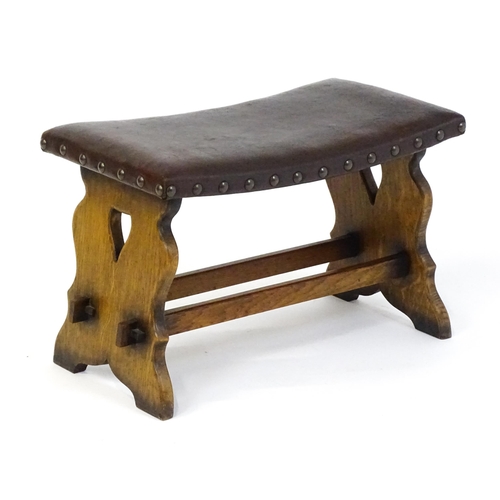 1487 - An early 20thC leather topped oak stool in the Gothic style with a studded upholstered top and trest... 