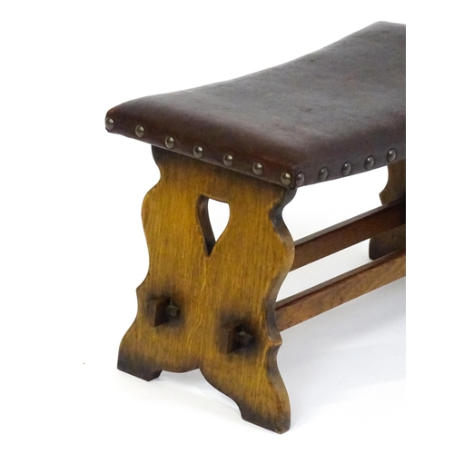 1487 - An early 20thC leather topped oak stool in the Gothic style with a studded upholstered top and trest... 