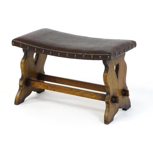 1487 - An early 20thC leather topped oak stool in the Gothic style with a studded upholstered top and trest... 