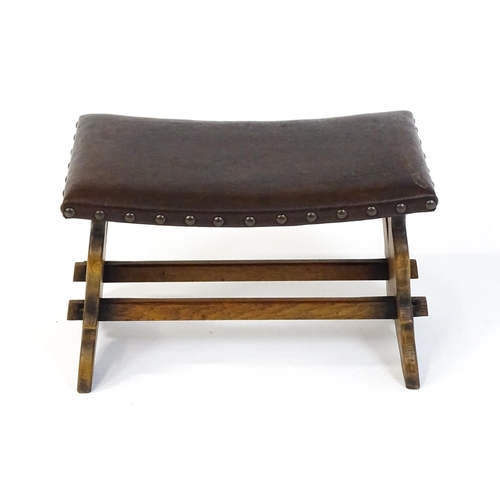 1487 - An early 20thC leather topped oak stool in the Gothic style with a studded upholstered top and trest... 