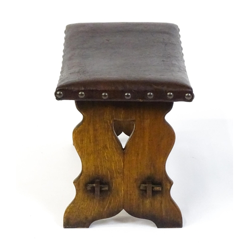 1487 - An early 20thC leather topped oak stool in the Gothic style with a studded upholstered top and trest... 