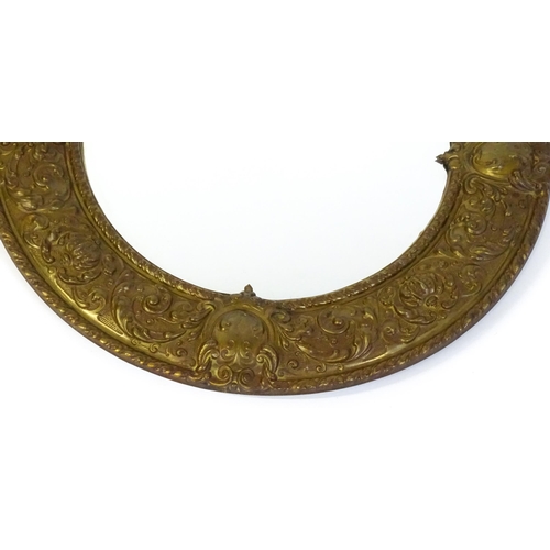 1482 - An early 20thC circular mirror with a brass embossed frame. 24