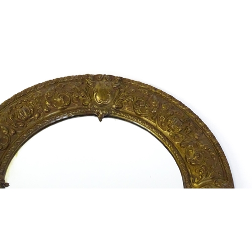 1482 - An early 20thC circular mirror with a brass embossed frame. 24