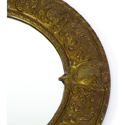 1482 - An early 20thC circular mirror with a brass embossed frame. 24