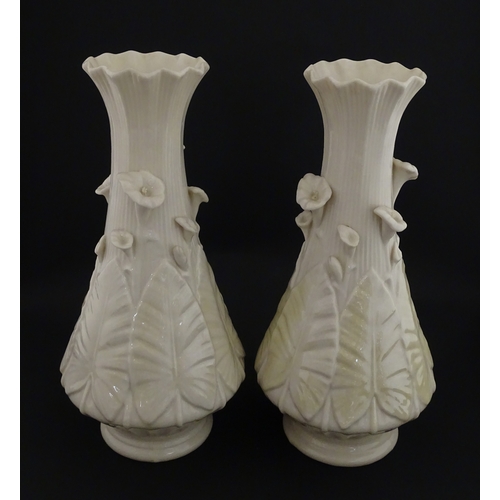 69 - A pair of Belleek vases in the Nile pattern having cala lily and foliate detail, with lustre highlig... 