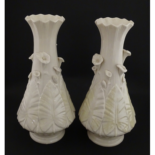 69 - A pair of Belleek vases in the Nile pattern having cala lily and foliate detail, with lustre highlig... 