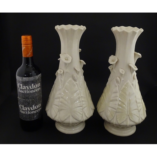 69 - A pair of Belleek vases in the Nile pattern having cala lily and foliate detail, with lustre highlig... 