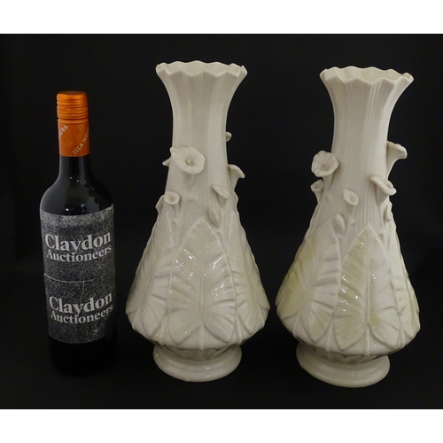69 - A pair of Belleek vases in the Nile pattern having cala lily and foliate detail, with lustre highlig... 
