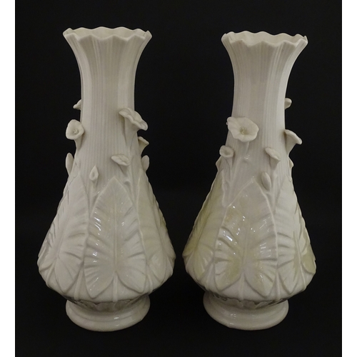 69 - A pair of Belleek vases in the Nile pattern having cala lily and foliate detail, with lustre highlig... 