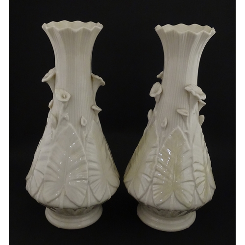 69 - A pair of Belleek vases in the Nile pattern having cala lily and foliate detail, with lustre highlig... 