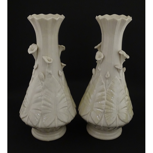 69 - A pair of Belleek vases in the Nile pattern having cala lily and foliate detail, with lustre highlig... 
