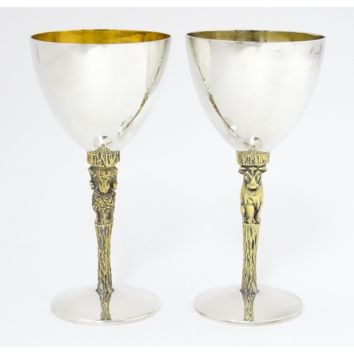 Stuart Devlin : A pair of limited edition Elizabeth II Modernist silver wine goblets with parcel gilt stems, one with bull decoration numbered 35, the other with ram decoration numbered 50, hallmarked 1977 / 78, maker Stuart Devlin. Produced for the Royal Agricultural Society. Approx. 6" high (2)