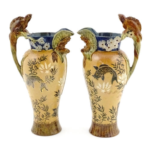 104 - A pair of Doulton Lambeth stoneware grotesque ewers / pitchers, the bodies decorated with carp fish ... 