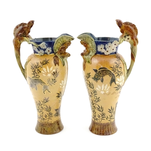 104 - A pair of Doulton Lambeth stoneware grotesque ewers / pitchers, the bodies decorated with carp fish ... 