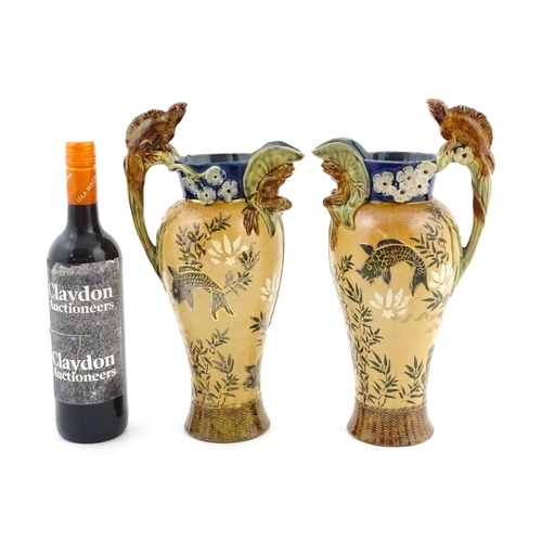 104 - A pair of Doulton Lambeth stoneware grotesque ewers / pitchers, the bodies decorated with carp fish ... 