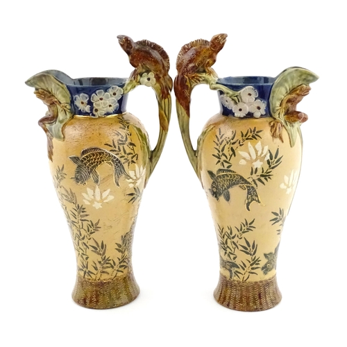 104 - A pair of Doulton Lambeth stoneware grotesque ewers / pitchers, the bodies decorated with carp fish ... 