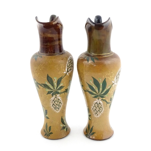 105 - A pair of Doulton Lambeth ewers / pitchers with stylised floral and foliate decoration by Lizzie Mar... 