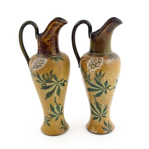 105 - A pair of Doulton Lambeth ewers / pitchers with stylised floral and foliate decoration by Lizzie Mar... 