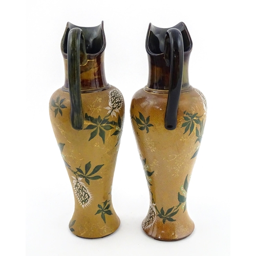 105 - A pair of Doulton Lambeth ewers / pitchers with stylised floral and foliate decoration by Lizzie Mar... 