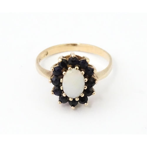 517 - A 9ct gold ring set with central opal bordered by blue spinels. Ring size approx. M