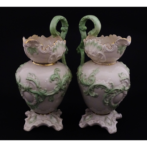 85 - A pair of Belleek jugs of shaped form with scrolling foliate decoration and green highlights. Both m... 