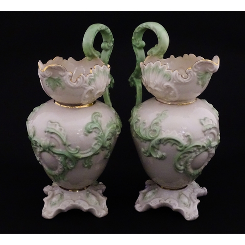 85 - A pair of Belleek jugs of shaped form with scrolling foliate decoration and green highlights. Both m... 