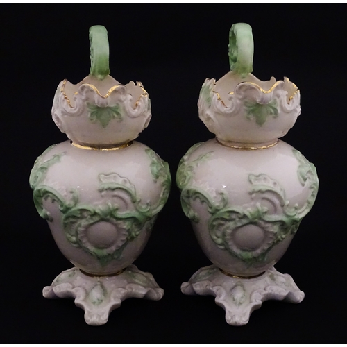 85 - A pair of Belleek jugs of shaped form with scrolling foliate decoration and green highlights. Both m... 