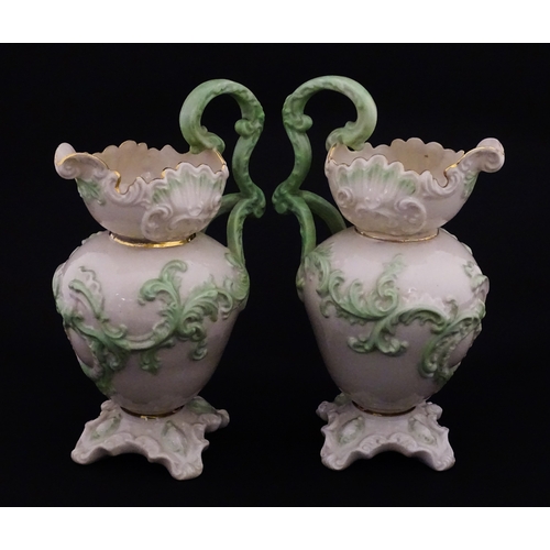 85 - A pair of Belleek jugs of shaped form with scrolling foliate decoration and green highlights. Both m... 