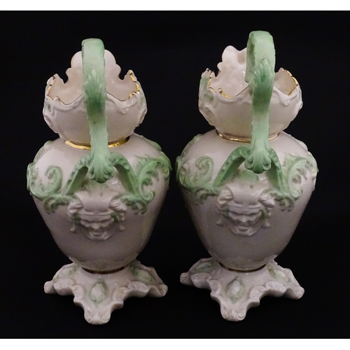 85 - A pair of Belleek jugs of shaped form with scrolling foliate decoration and green highlights. Both m... 